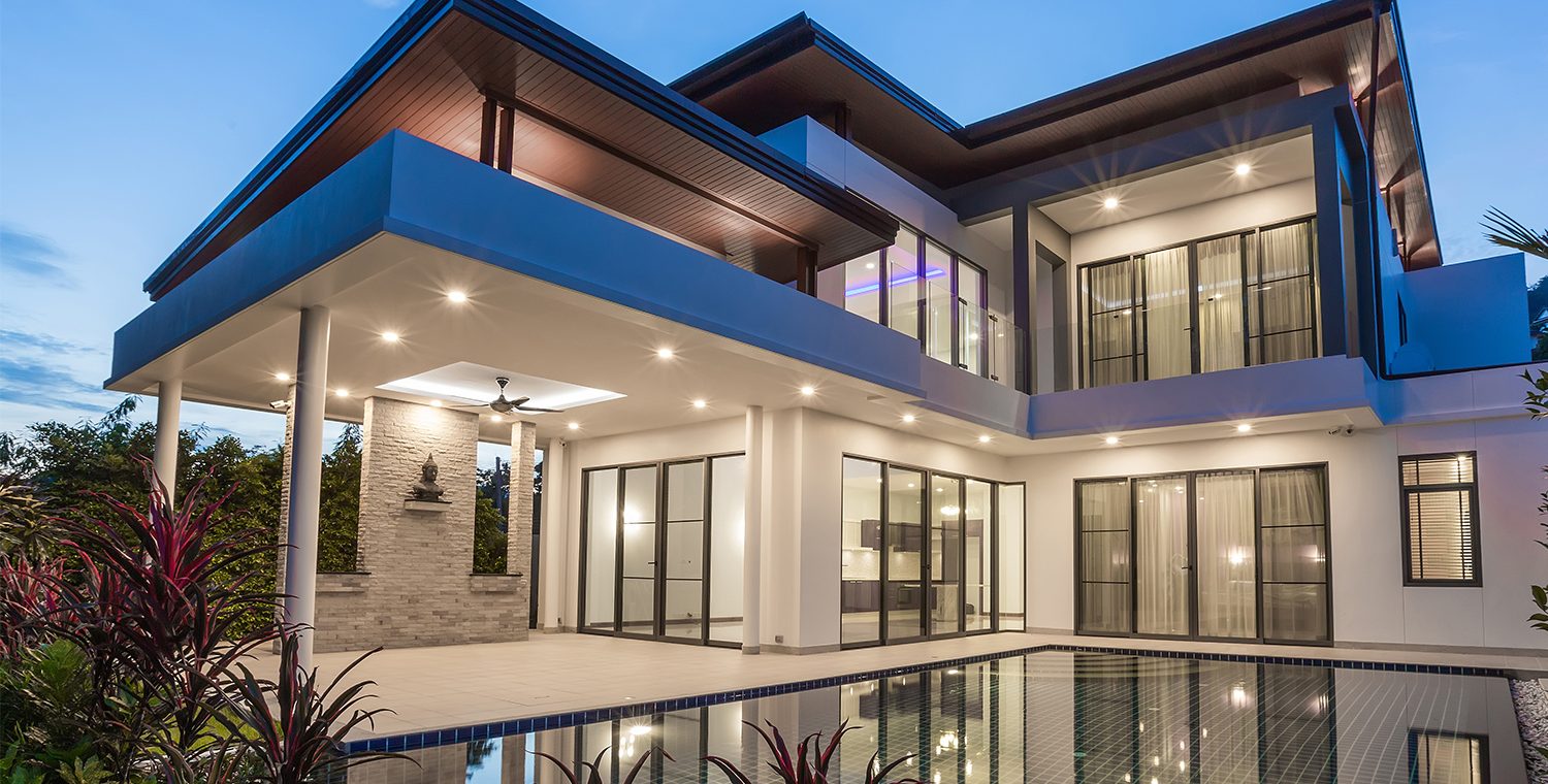 Modern luxury home at dusk with pool and warm interior lighting